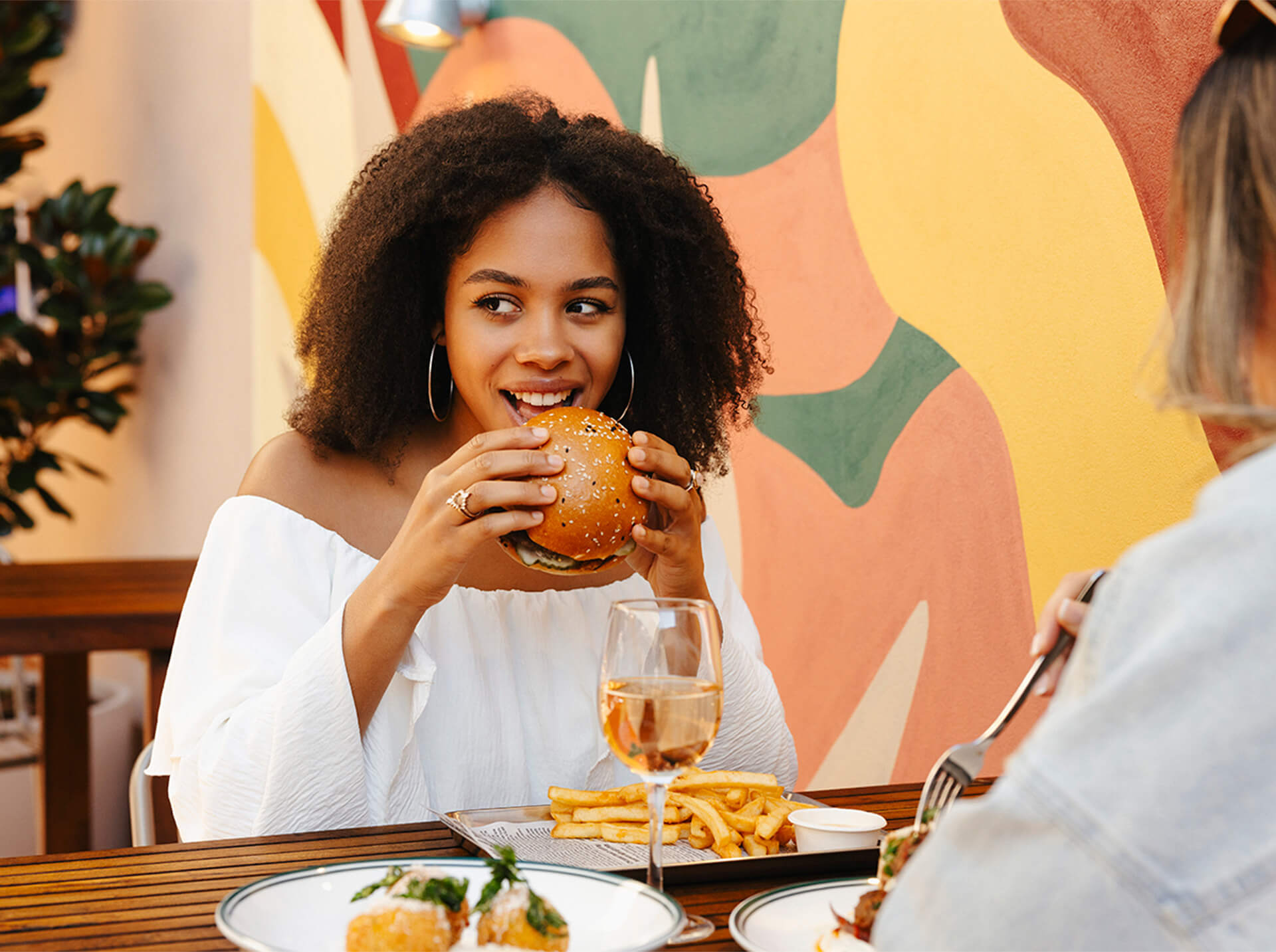 A woman enjoying a delicious burger and fries at a restaurant, savouring every bite with a smile on her face.