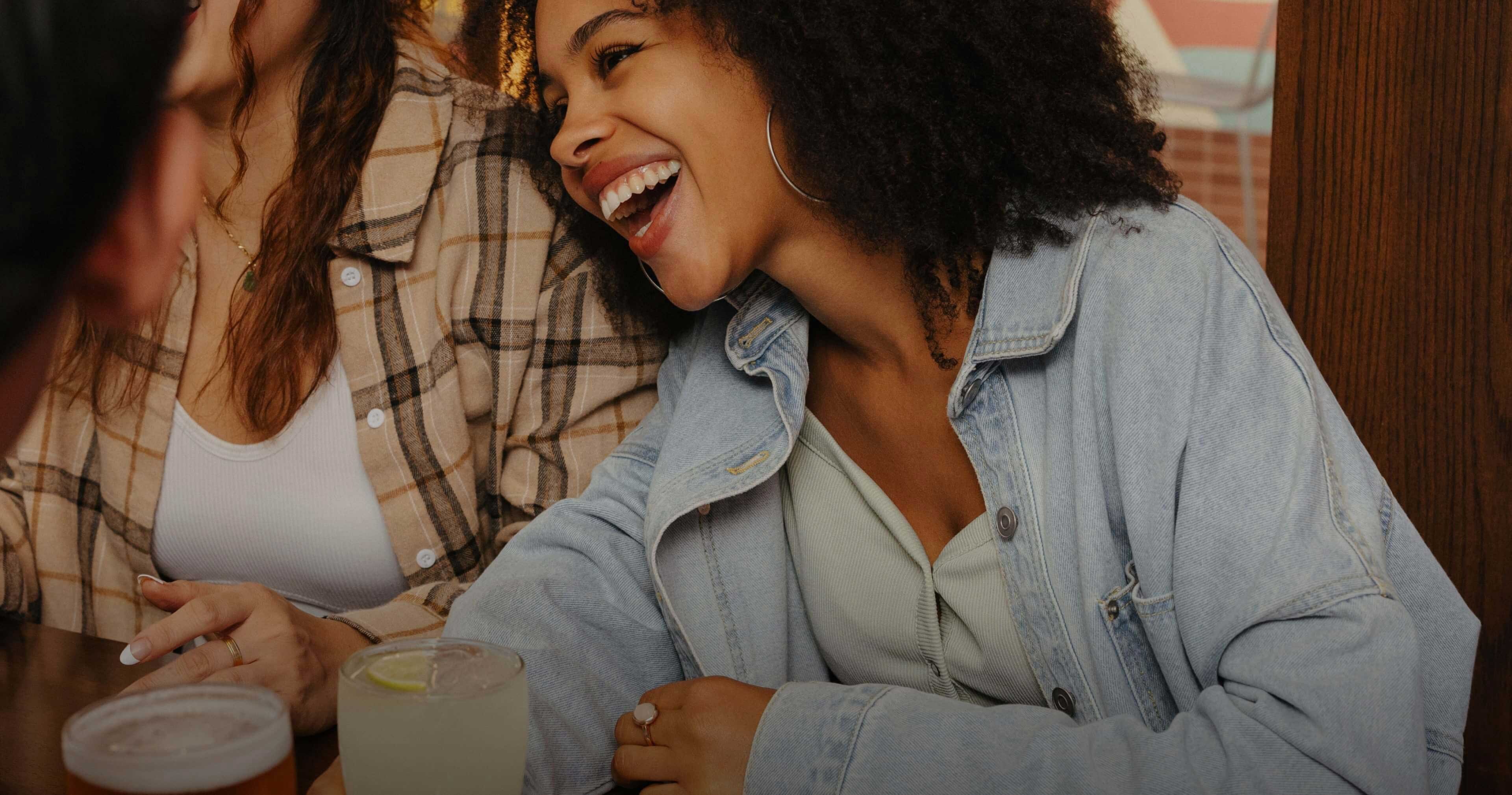 Two women enjoying drinks at a table, one woman smiling with friends.
